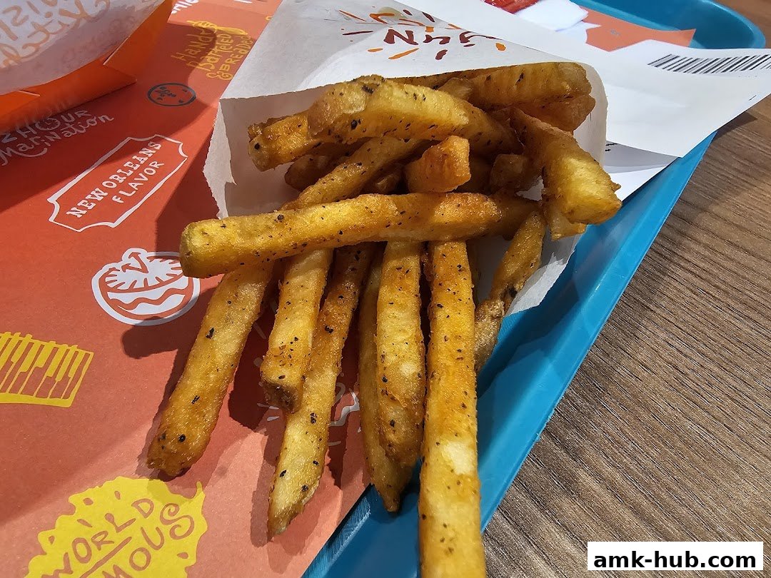 A close-up shot of Popeyes' signature seasoned fries served in a paper bag on a blue tray.