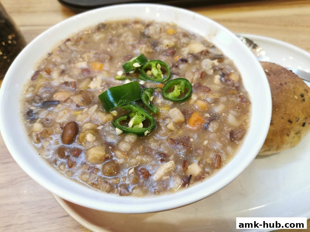 A hearty bowl of mixed grain soup topped with sliced green chilies and a side of bread.