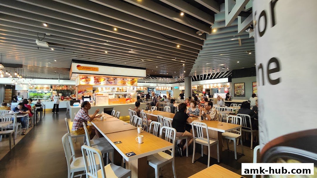 A busy food court with people dining at tables and various food stalls in the background.