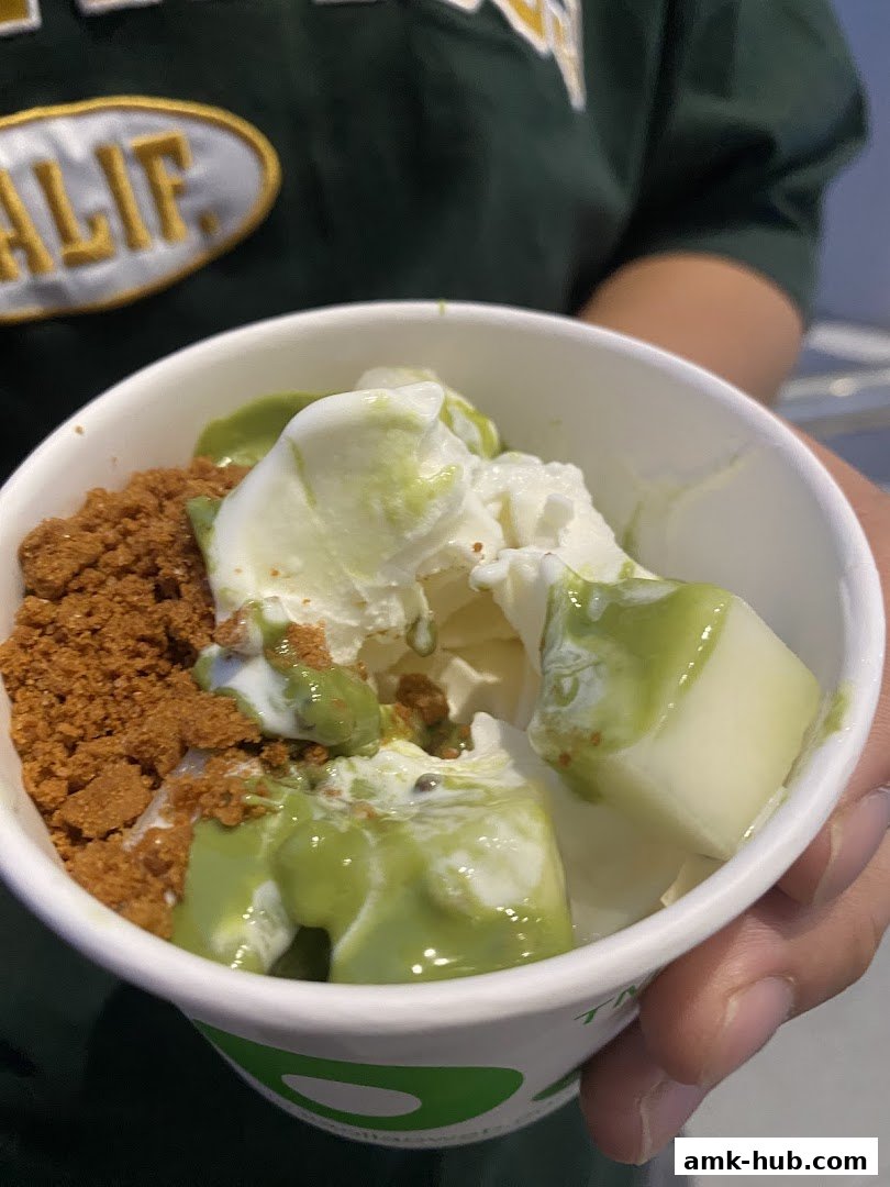A cup of frozen yogurt with green sauce and cookie crumbles.