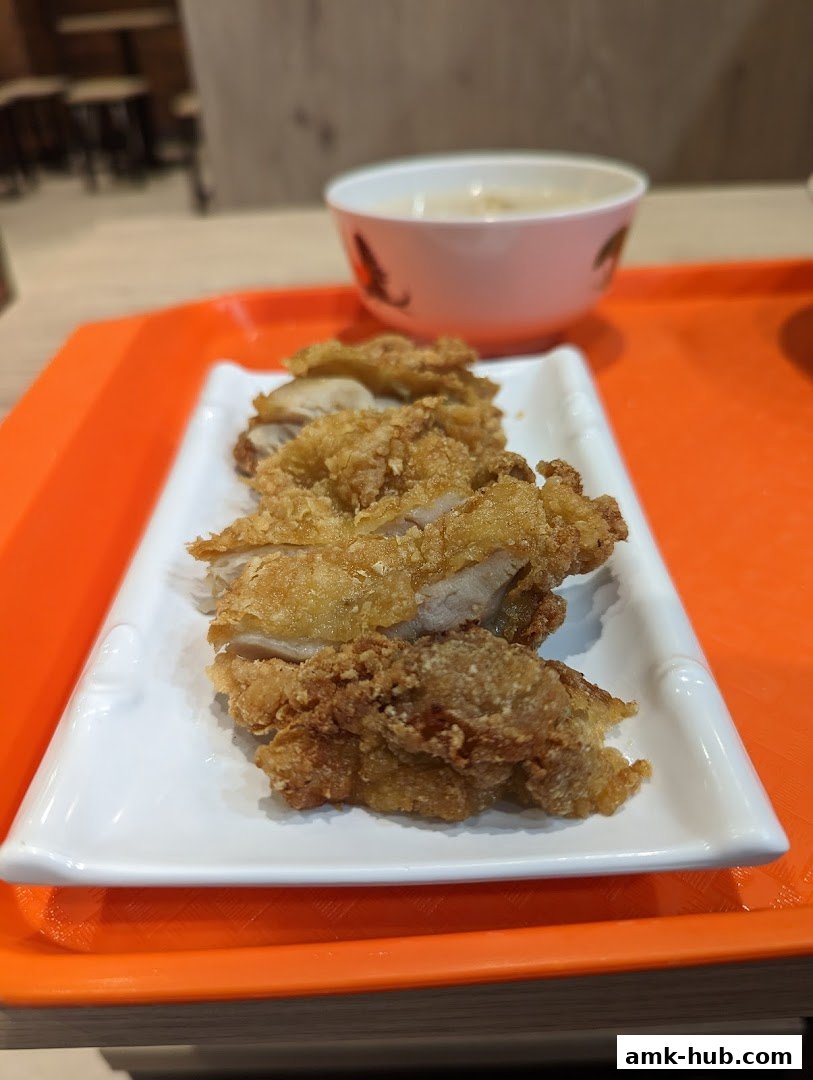 A plate of crispy fried chicken pieces served with a bowl of soup on an orange tray.