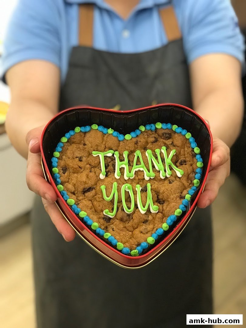 A person holds a heart-shaped cookie with 'Thank You' written in icing.