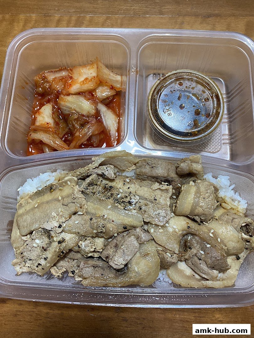A takeaway container filled with rice, grilled meat, kimchi, and dipping sauce.