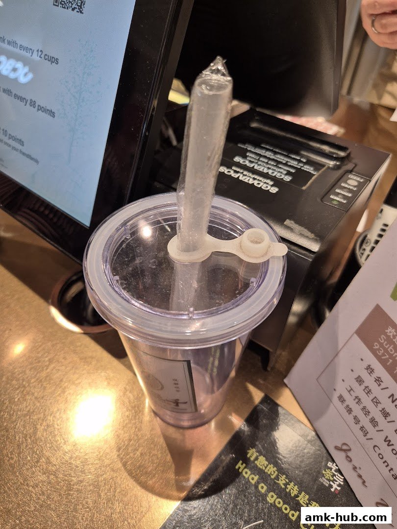 A close-up of a bubble tea cup with a straw at a counter, next to a receipt printer.