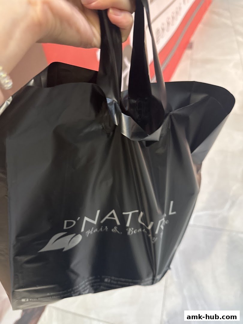 A hand holds a black shopping bag with the D'NATURAL Hair & Beauty logo.