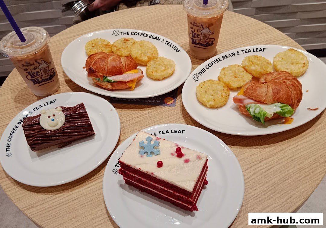 A table laden with coffee drinks, croissant sandwiches, and two slices of cake.