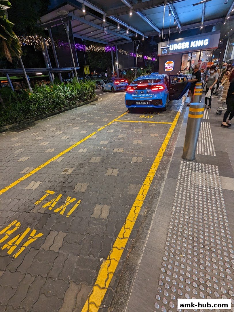 A taxi stand outside a Burger King with taxis waiting and people queuing.