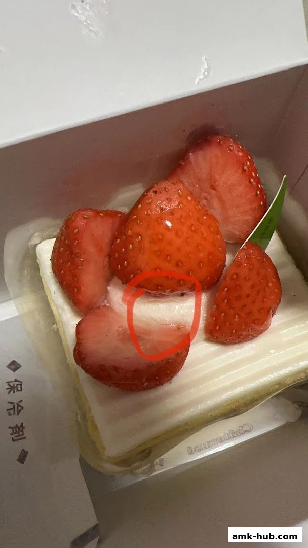 A slice of strawberry cake with fresh strawberries on top, presented in a white box.