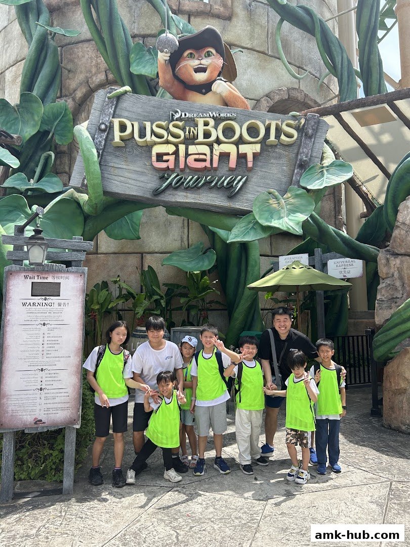 A group of children and an adult pose for a photo in front of the Puss in Boots Giant Journey attraction.