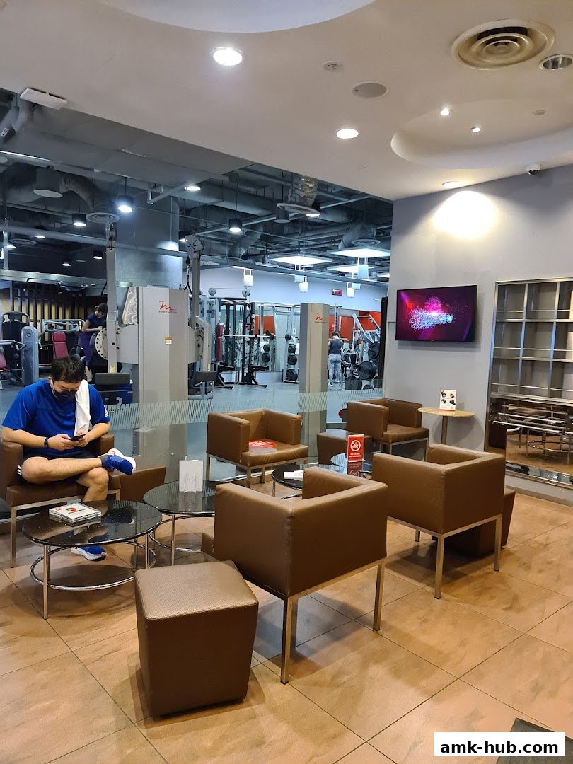 A man sits in a lounge area of a gym, with workout equipment visible in the background.