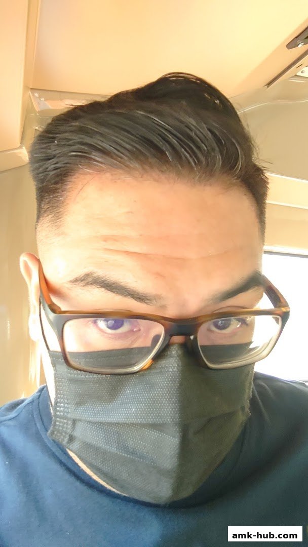 A close-up of a person wearing glasses and a face mask, with styled hair.