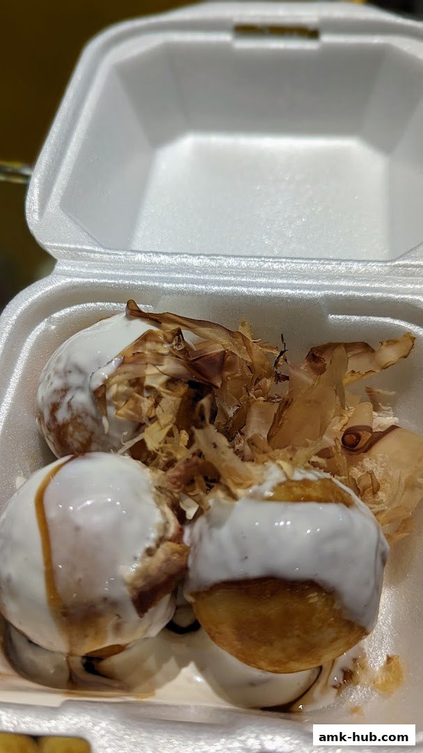 A close-up of takoyaki balls topped with sauce and bonito flakes in a takeout container.