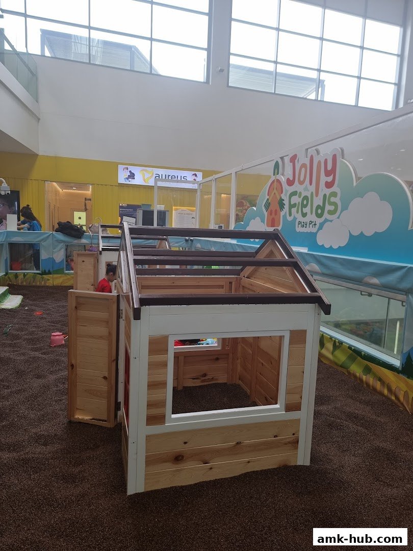 A wooden playhouse sits in a ball pit area with colorful signage in the background.