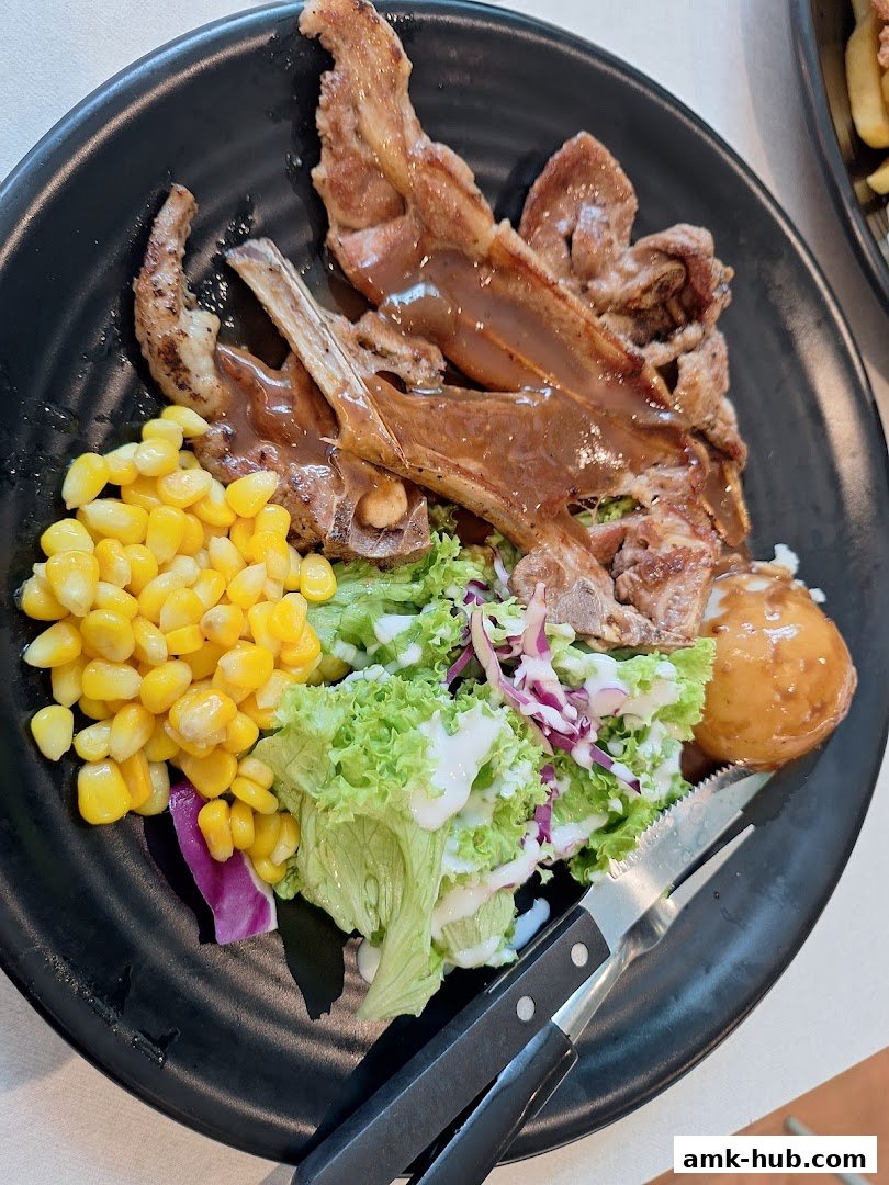 A plate of lamb chops with corn, salad, and a potato, served with cutlery.