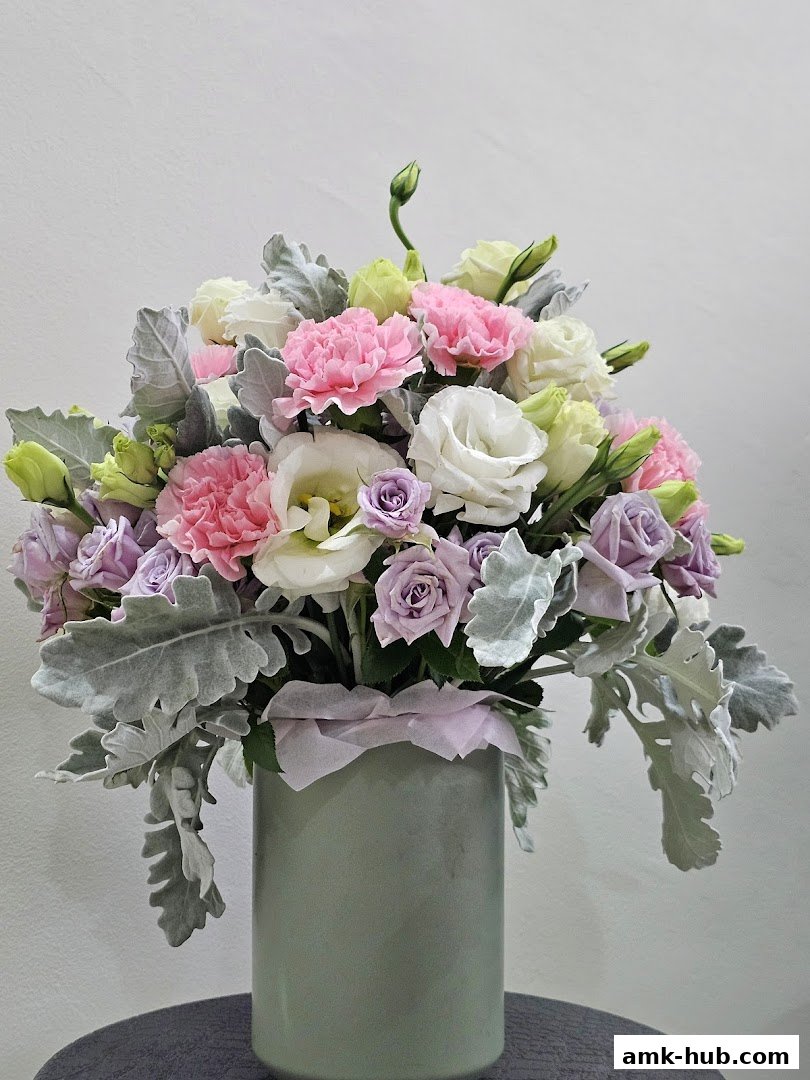 A beautiful floral arrangement in a sage green vase with pink, white, and purple flowers.