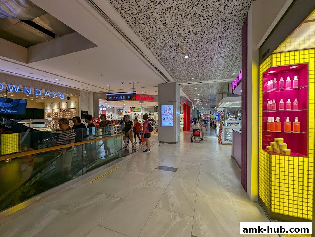 A bustling shopping mall interior with various shops and shoppers on escalators.