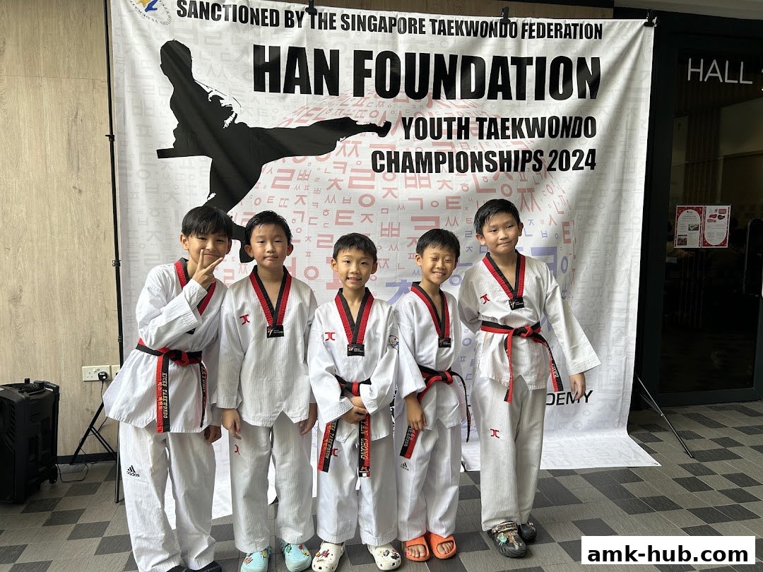 Five young boys in Taekwondo uniforms pose in front of a banner for the Han Foundation Youth Taekwondo Championships.