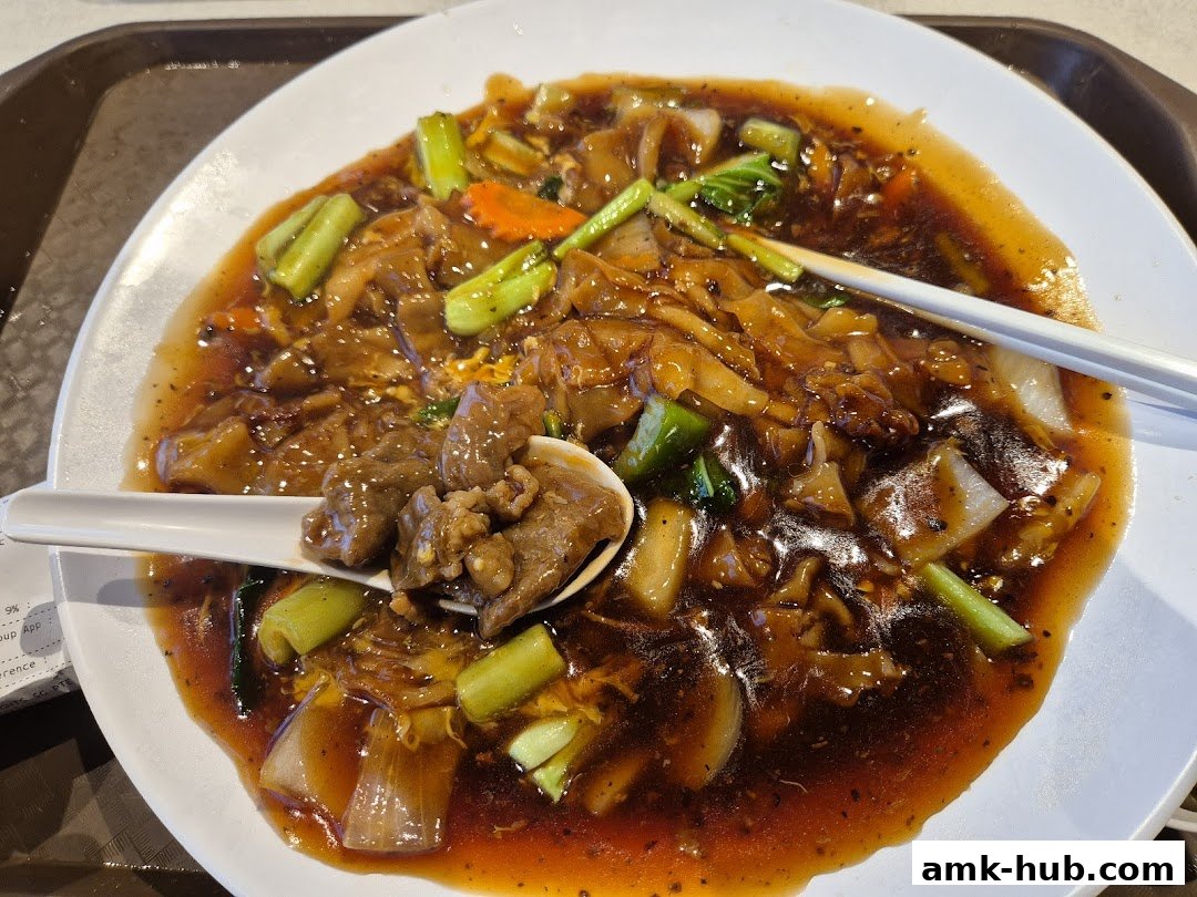 A close-up shot of a delicious plate of beef hor fun with chopsticks and a spoon.