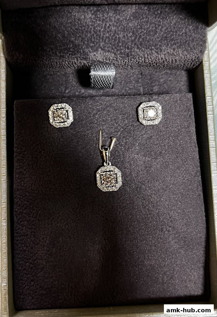 A jewelry set featuring a pendant and earrings with diamonds in a presentation box.