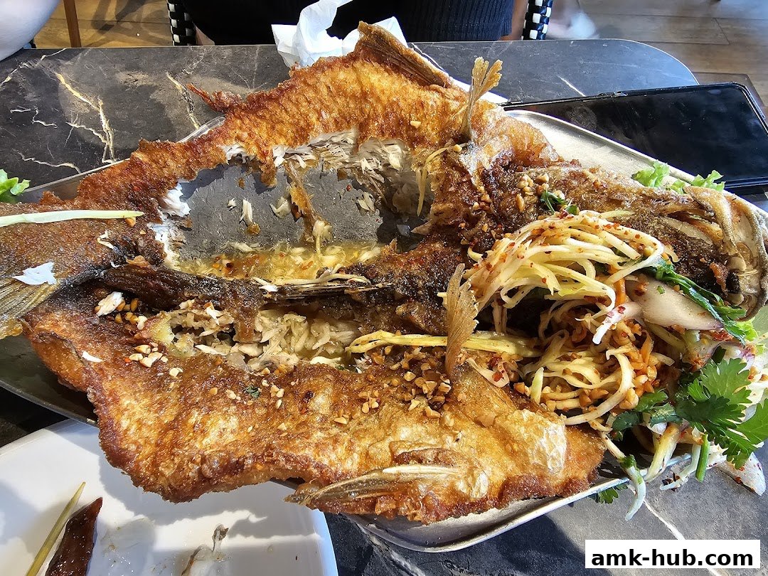 A whole fried fish served with a fresh mango salad and garnished with herbs.