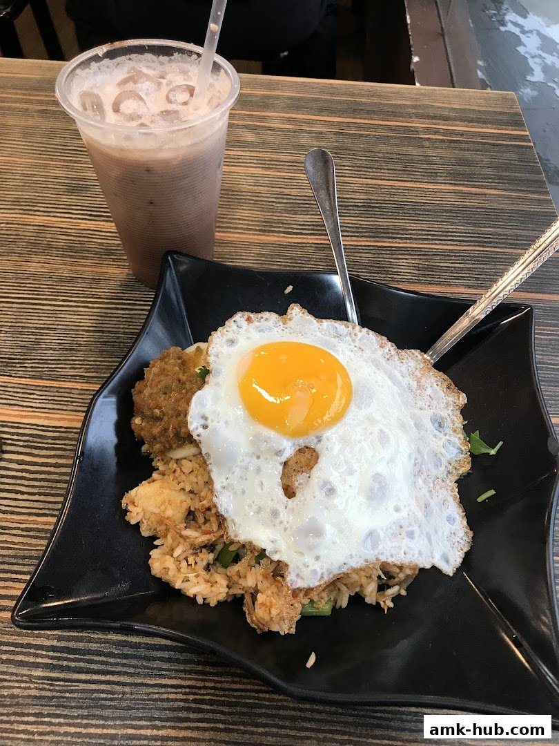 A plate of fried rice topped with a sunny-side-up egg and a side of meat, with a drink.