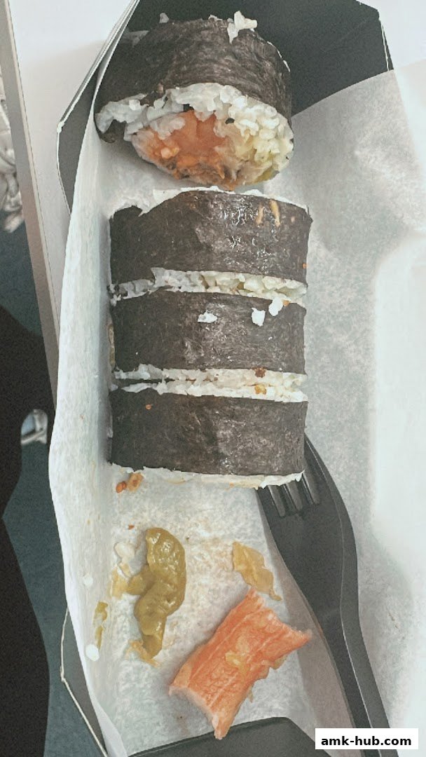 A close-up of sushi rolls in a takeaway container with a fork and some condiments.