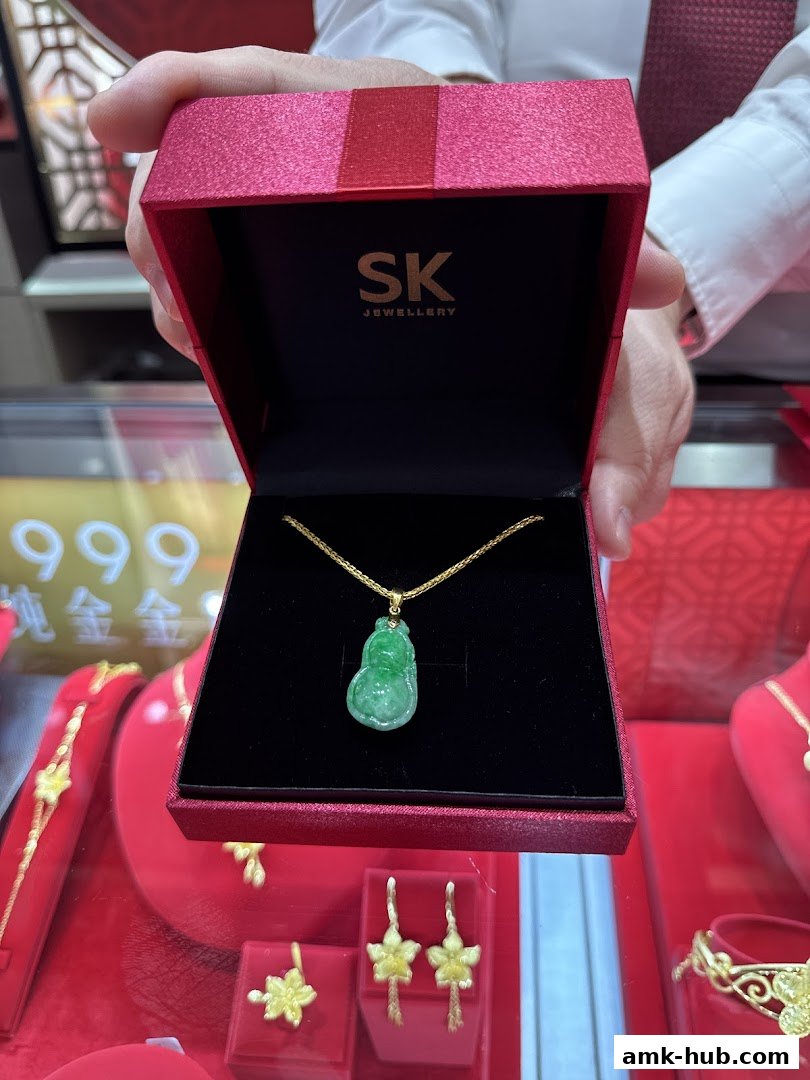 A person holds open a red gift box revealing a jade pendant necklace from SK Jewellery.