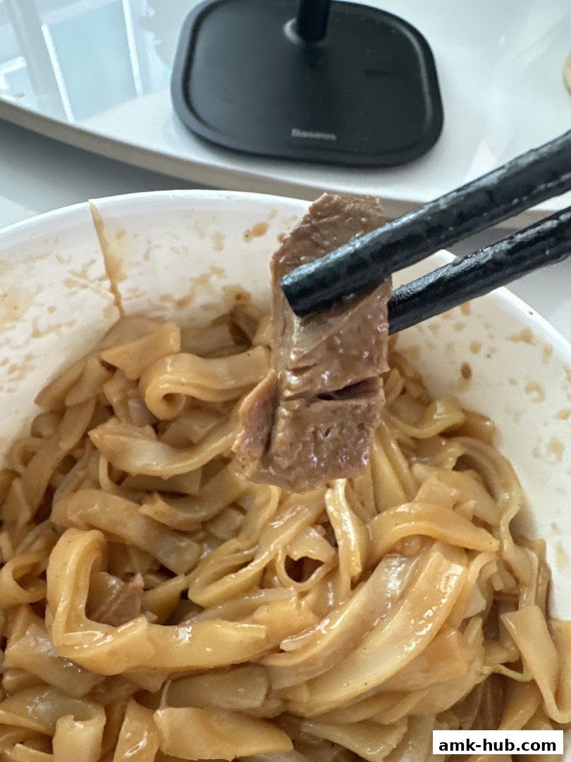 A close-up shot of noodles and meat being picked up with chopsticks.