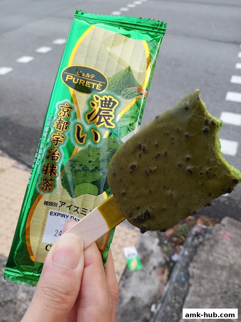 A hand holds a bitten matcha ice cream bar with Japanese packaging.
