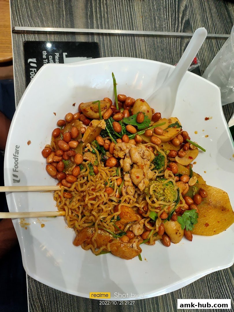 A bowl of spicy noodles with chicken, peanuts, broccoli, and potatoes, served with chopsticks.