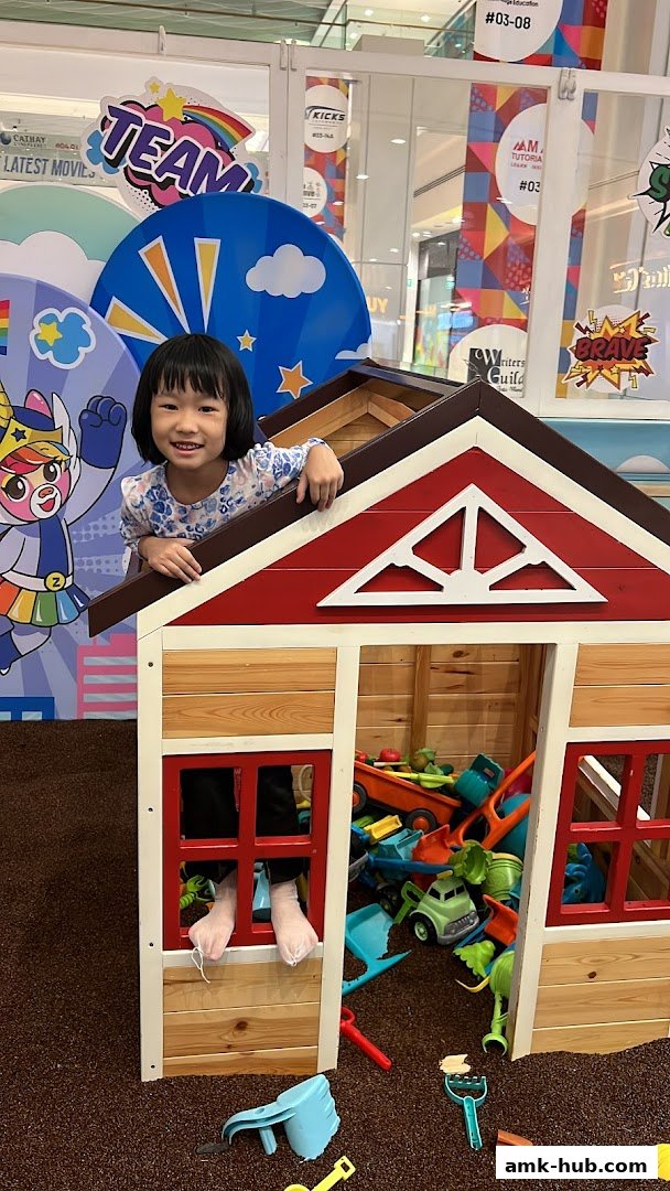 A happy child peeks out of a wooden playhouse filled with toys.