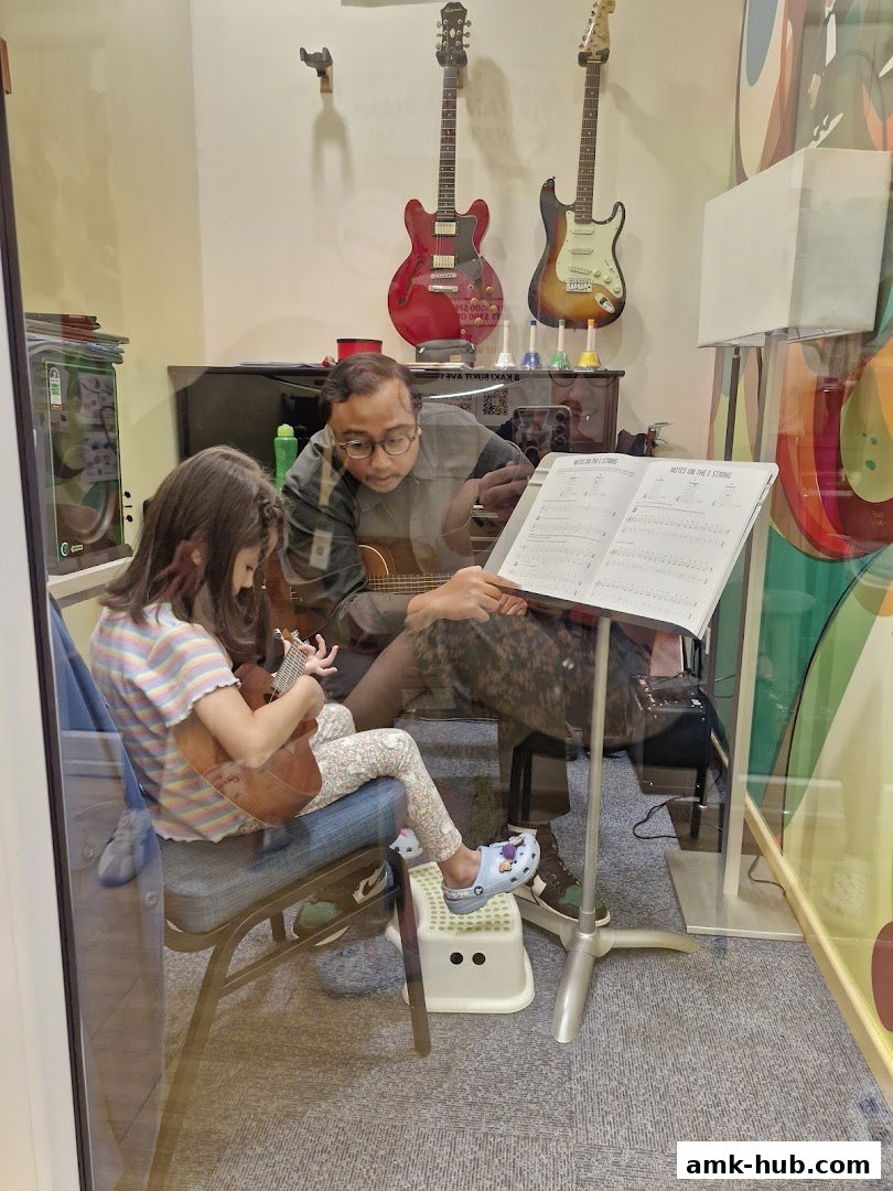 A music teacher instructs a young student on the ukulele in a classroom setting.