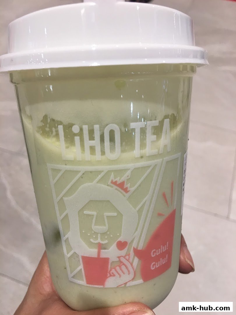 A hand holds a LiHO TEA cup filled with a light green beverage.
