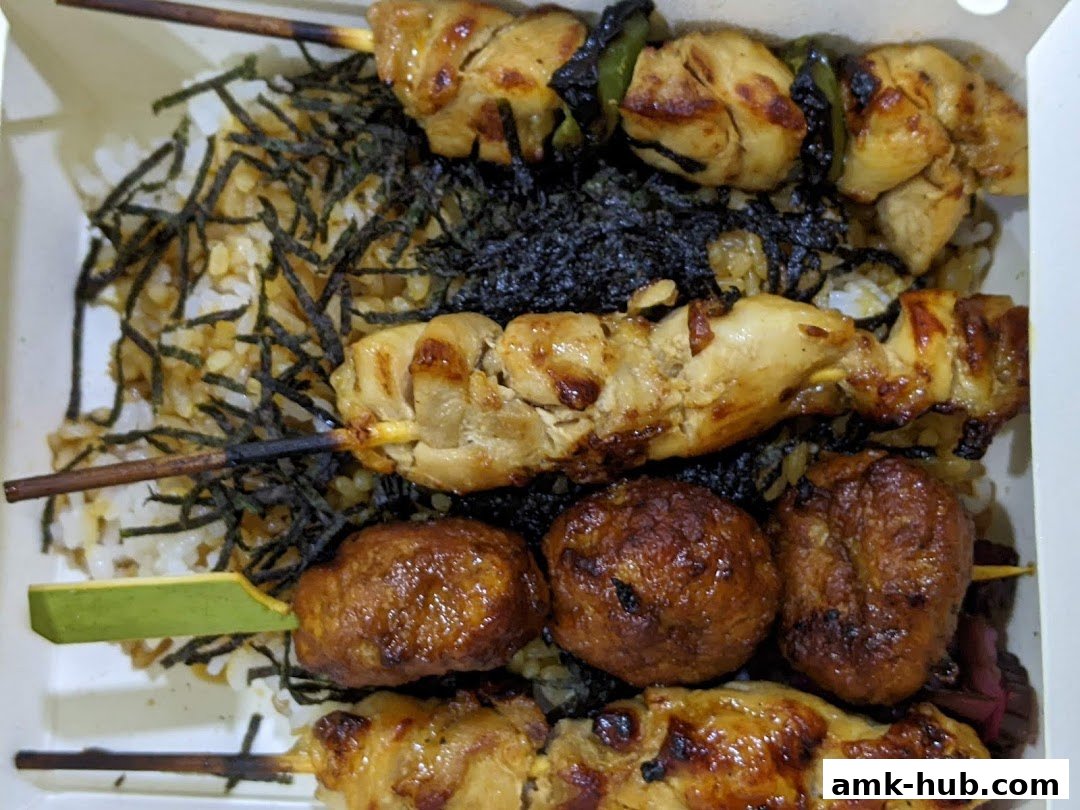 A close-up of a takeaway box filled with grilled chicken skewers and rice topped with seaweed.