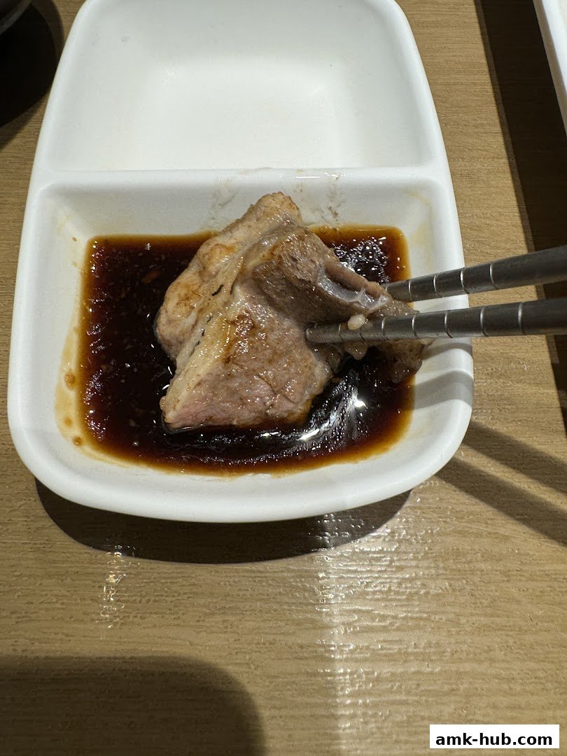 A piece of grilled meat is being dipped into a sauce with chopsticks.