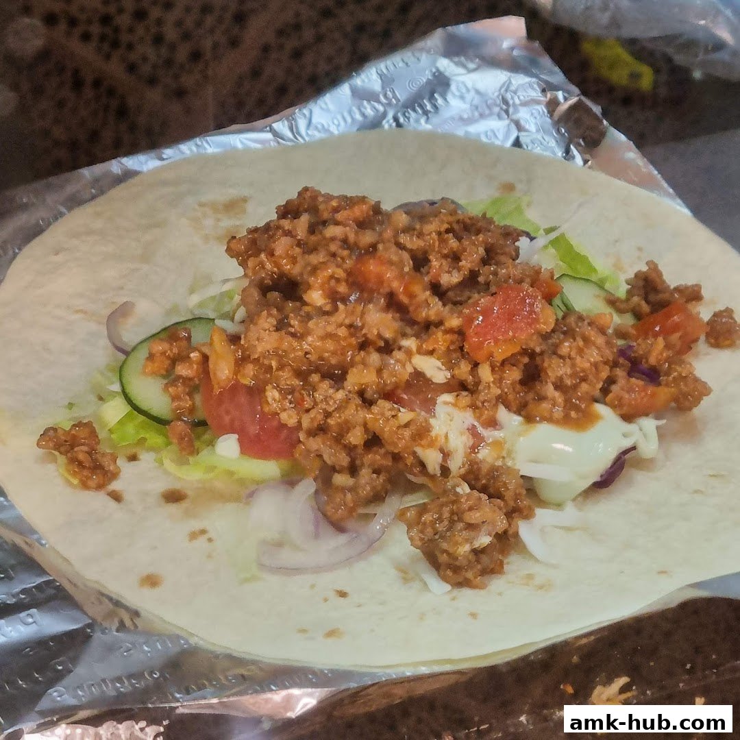 A close-up of a freshly made wrap filled with seasoned ground meat, lettuce, tomatoes, and onions.
