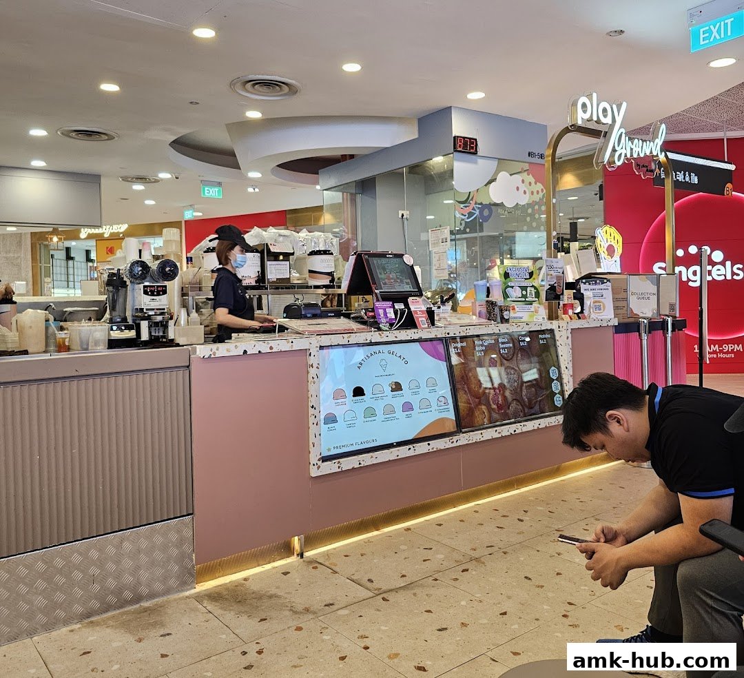 A gelato shop counter with a staff member and digital displays showing flavors and prices.
