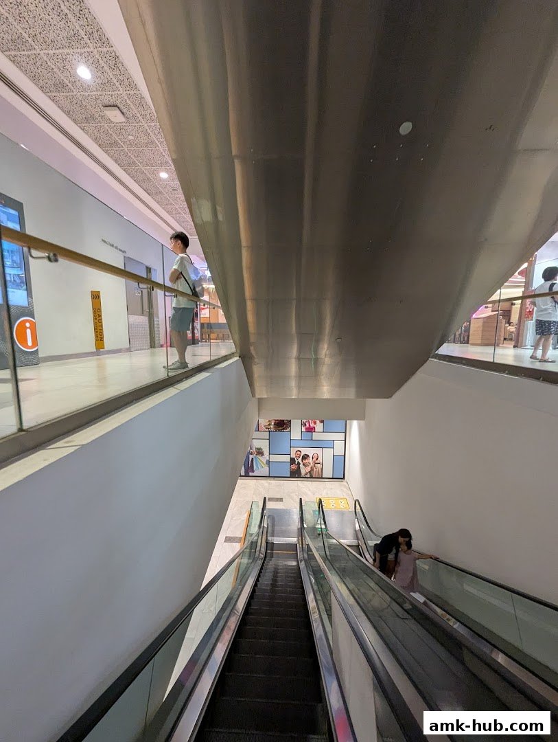 People on escalators in a modern shopping mall with a large metallic overhang.