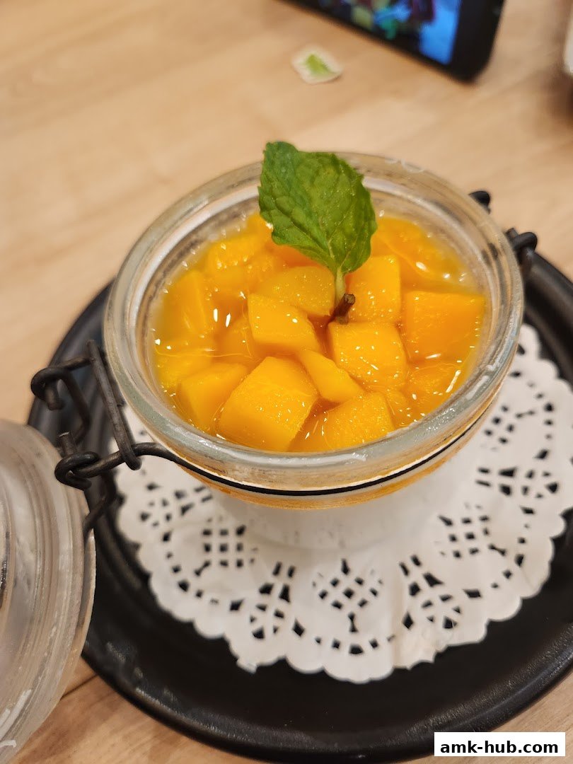 A close-up of a refreshing mango dessert in a glass jar, garnished with mint.