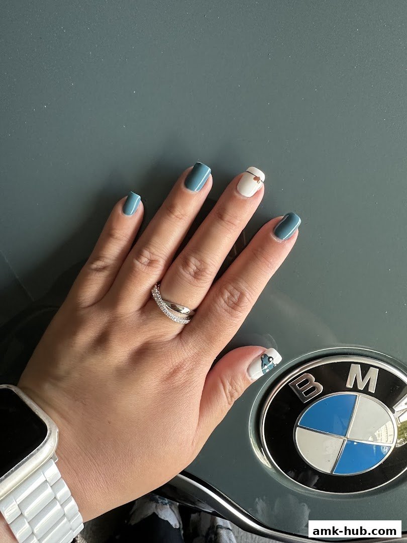 A hand with stylish blue and white nails, wearing a ring and a watch, rests on a surface with a BMW logo.