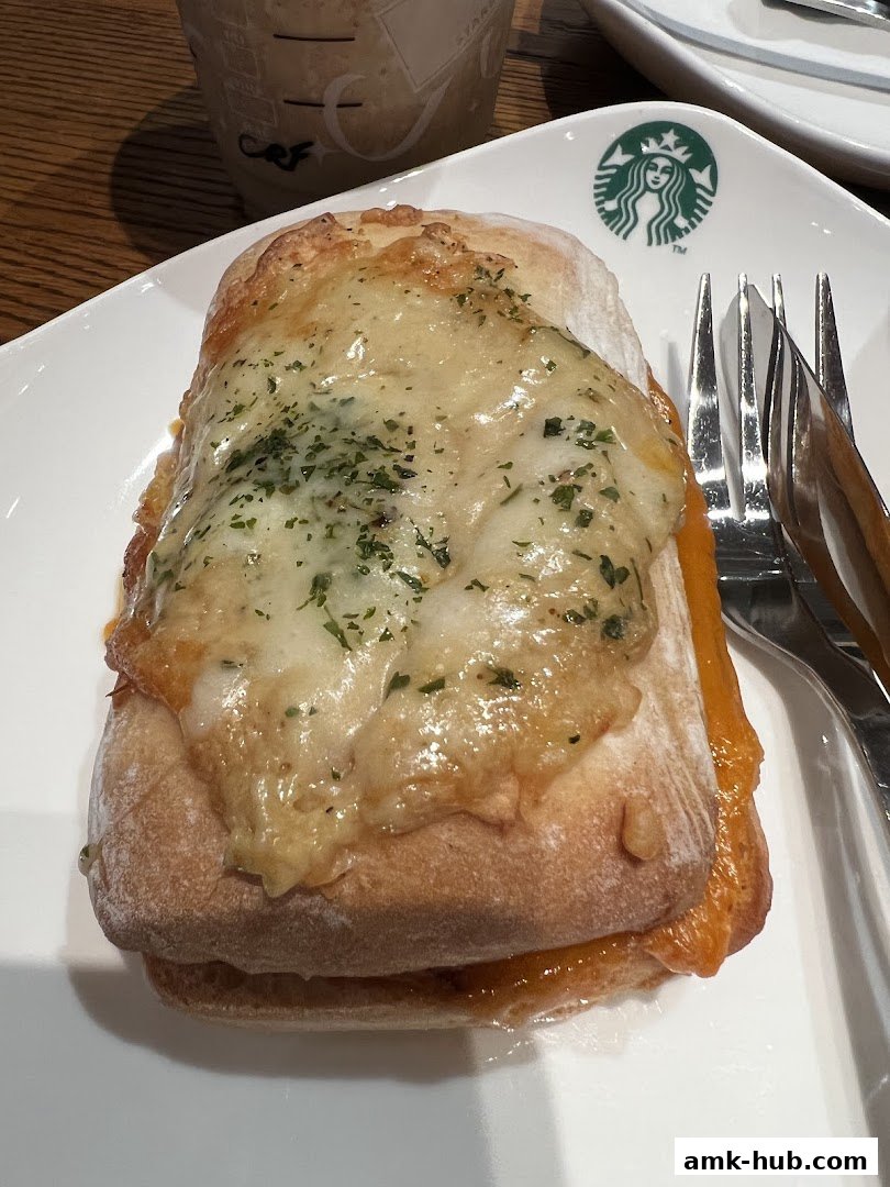 A close-up of a savory pastry with melted cheese and herbs, served on a white plate with forks.