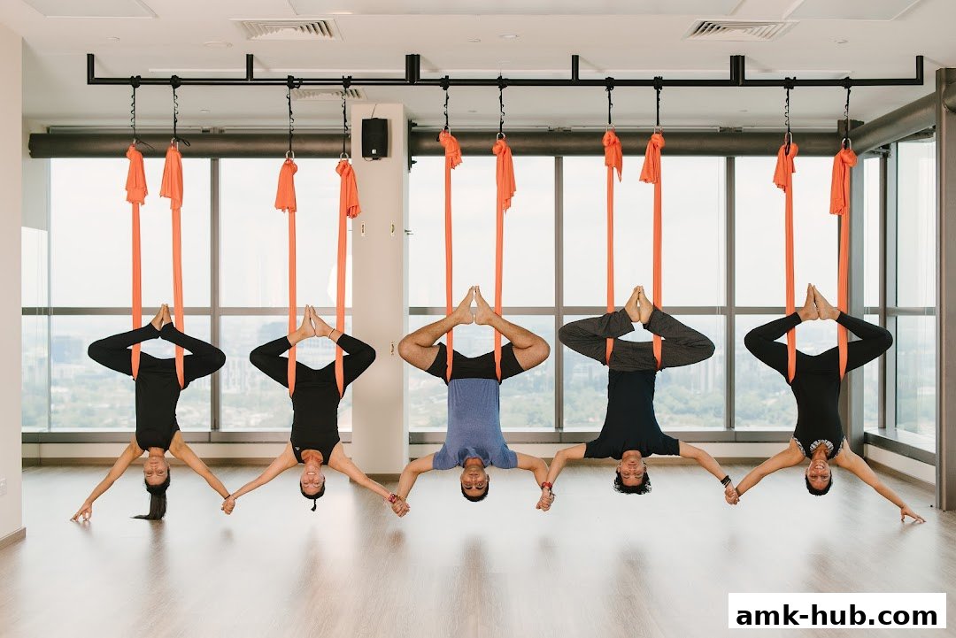 Five people are doing aerial yoga, suspended upside down in orange hammocks.
