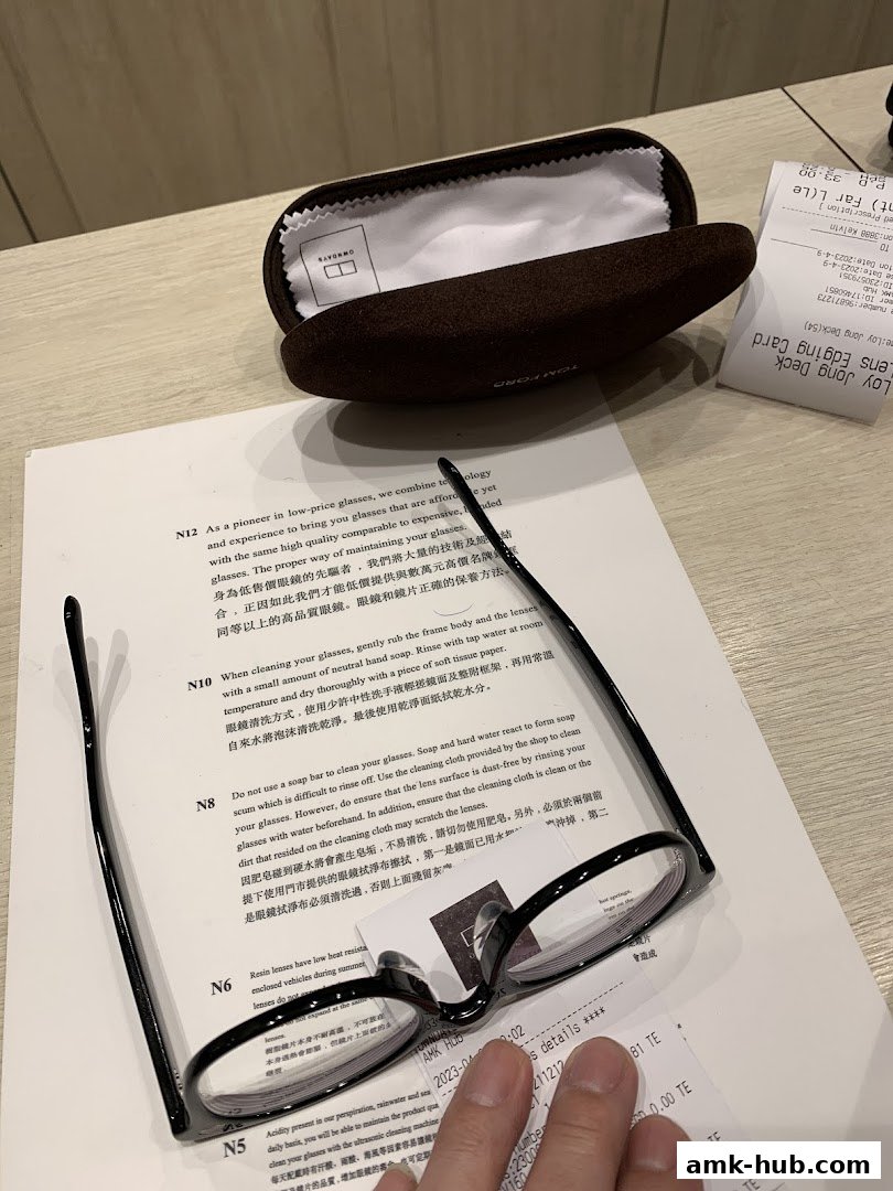 A pair of black-rimmed glasses, a glasses case, and receipts are laid out on a table.