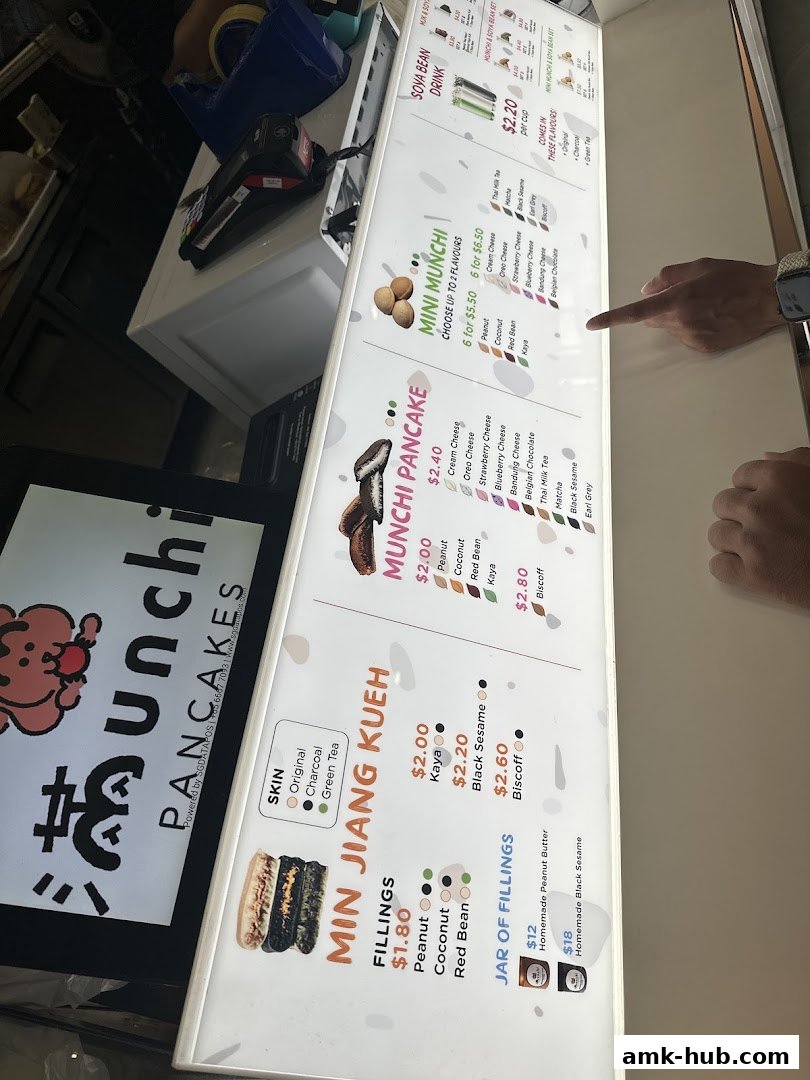 A brightly lit menu board for Munchi Pancakes, displaying various pancake and kueh options.