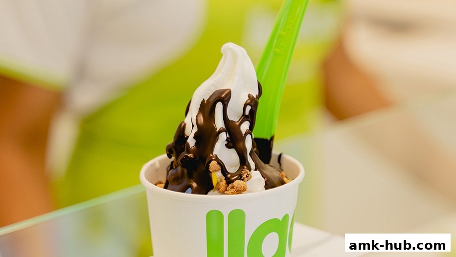 A cup of frozen yogurt with chocolate sauce and toppings, served with a green spoon.