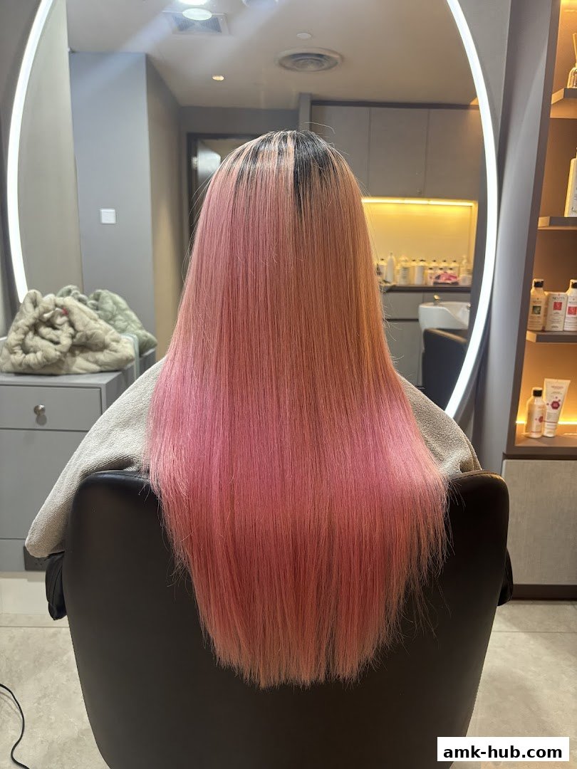 A person with long, straight, pink-dyed hair sitting in a salon chair.