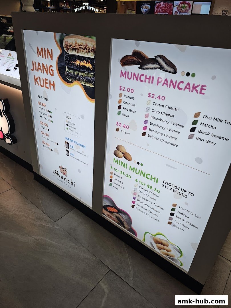 A brightly lit menu board for Munchi Pancakes and Min Jiang Kueh with various fillings and flavors.