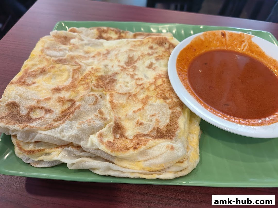 A close-up of flaky Roti Canai served with a side of curry on a green plate.