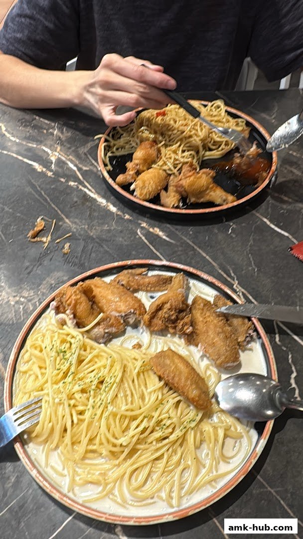 Two plates of spaghetti with fried chicken wings served on a marble-patterned table.