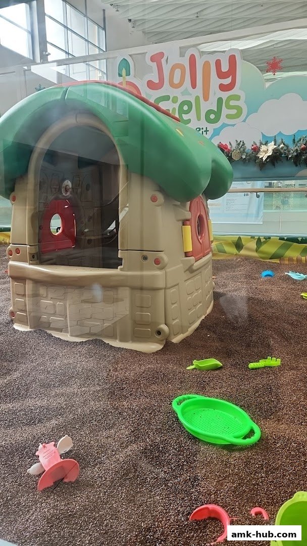 A colorful playhouse in a sandpit with various toys scattered around.